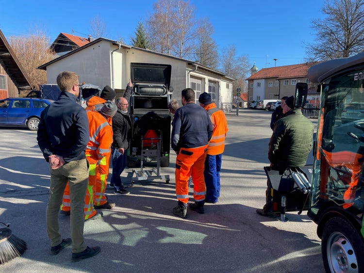Mehrere Personen in Arbeitskleidung beobachten eine Egholm Kommunalmaschine mit Kehrbesen