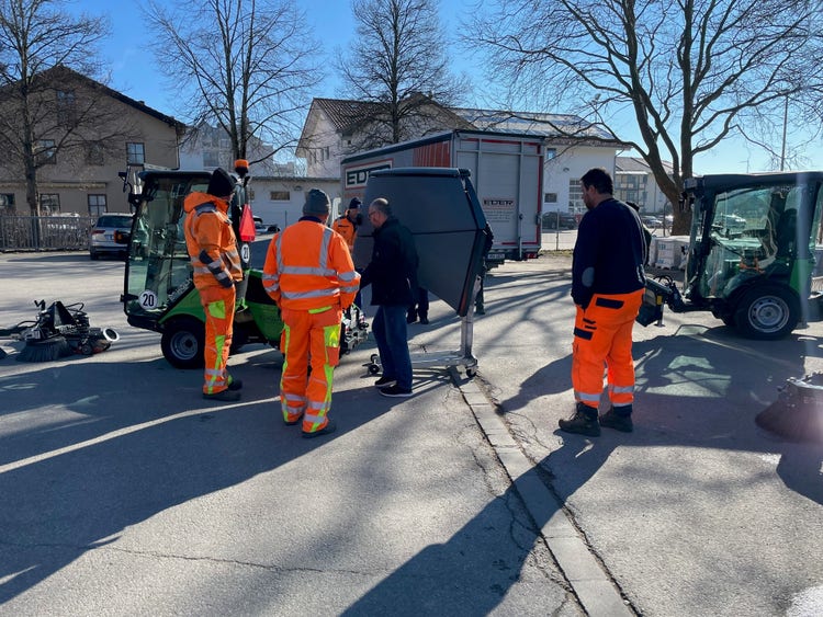 Mehrere Personen in Arbeitskleidung beobachten eine Egholm Kommunalmaschine mit Kehrbesen