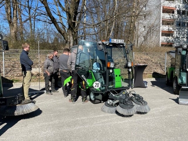 Mehrere Personen stehen um eine Egholm Kommunalmaschine mit Kehrbesen