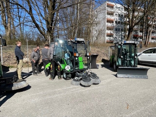 Mehrere Personen stehen um eine Egholm Kommunalmaschine mit Kehrbesen