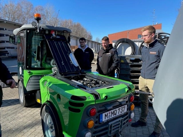 Mehrere Personen begutachten eine geöffnete grüne Egholm Kommunalmaschine auf einem Betriebshof