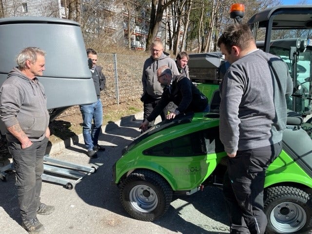 Eine Gruppe von Personen betrachtet die geöffnete Motorhaube einer grünen Egholm Kommunalmaschine