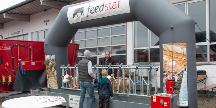 feedstar Messestand mit aufblasbarem Torbogen, Aussteller präsentiert Fütterungssystem mit Kuh-Attrappen, Besucher mit Kind informieren sich über die Technik.